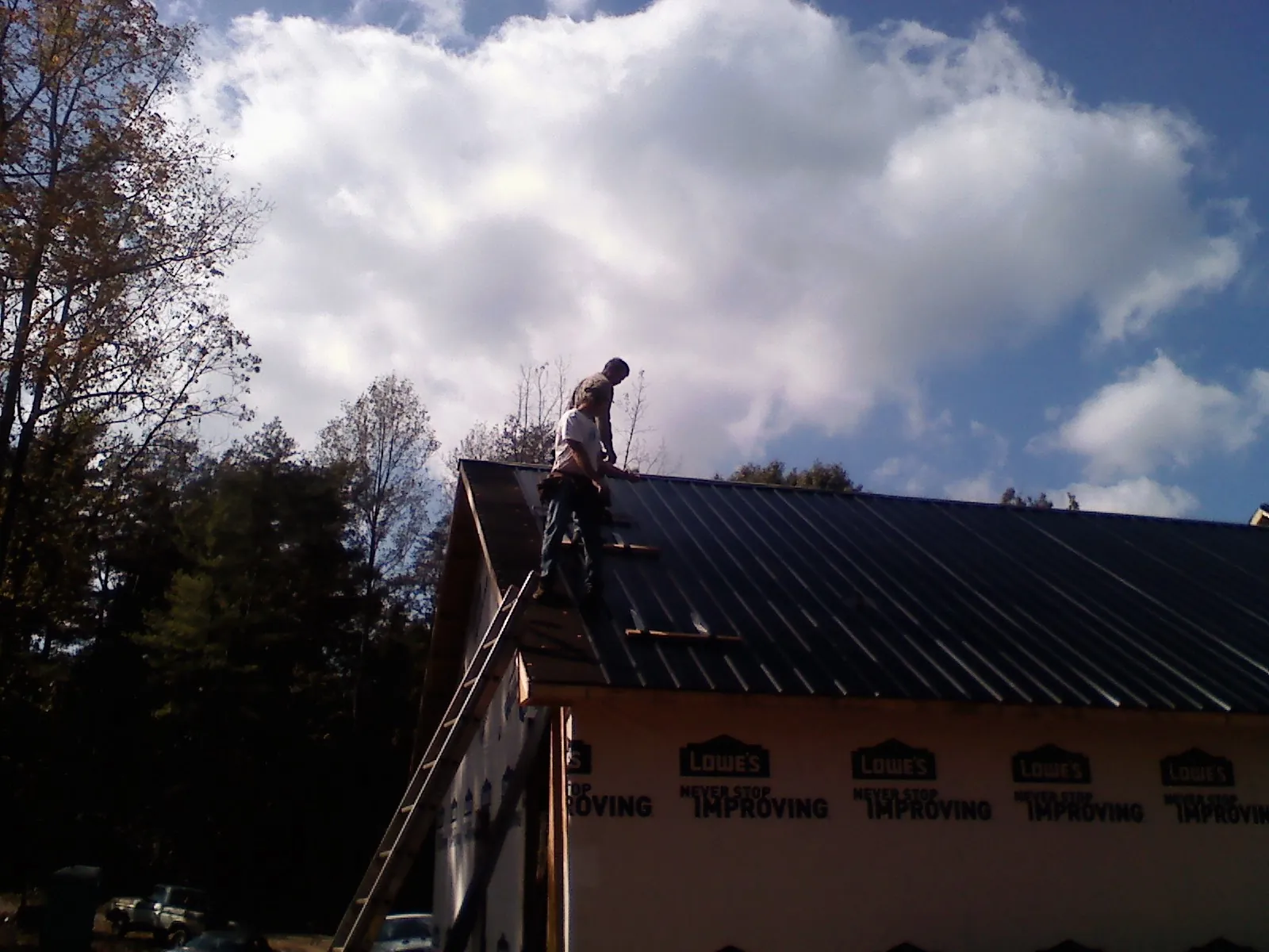 Roofer fastening dark metal panels high against a cloudy sky, from a Roof Inspection job in Garrett
