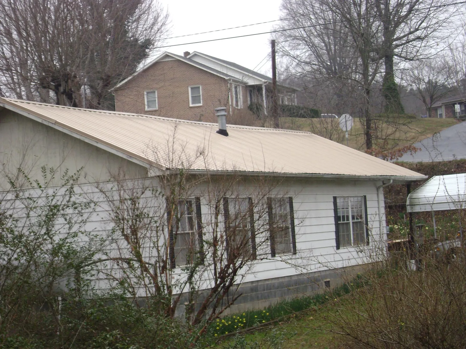 Tan metal roof on a white sided house set into a hillside — Commercial Roofing by Roofing Brothers in Garrett